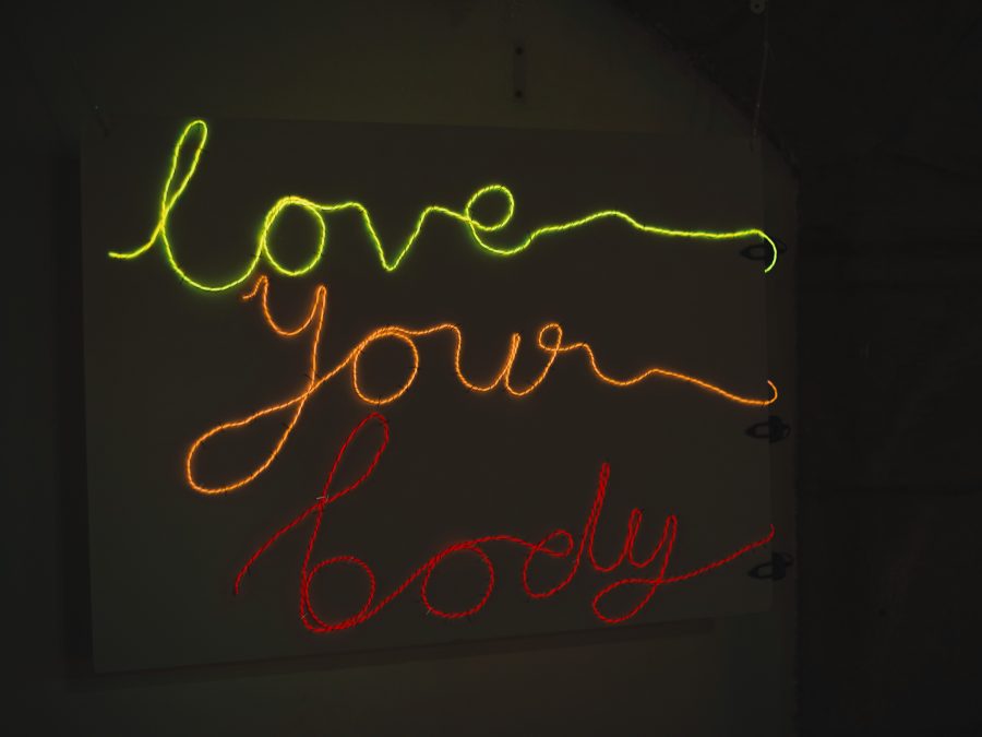 Image of three lines of text in neon colours reading 'Love Your Body' in loopy text