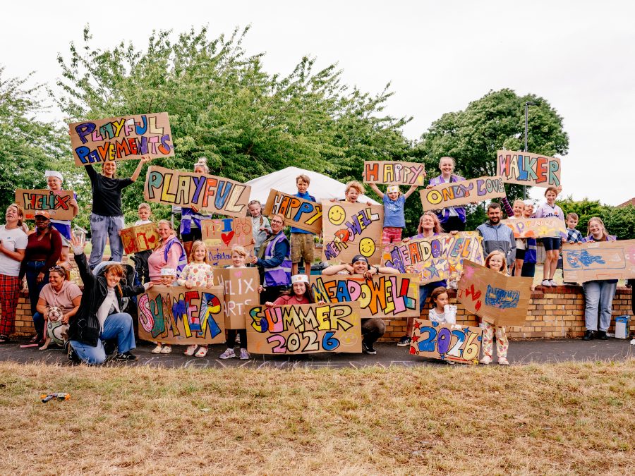 The community organisers and community participants of Playful Pavements holding colourful painted signs with phrases such as 'Playful Pavements' and Meadowell'